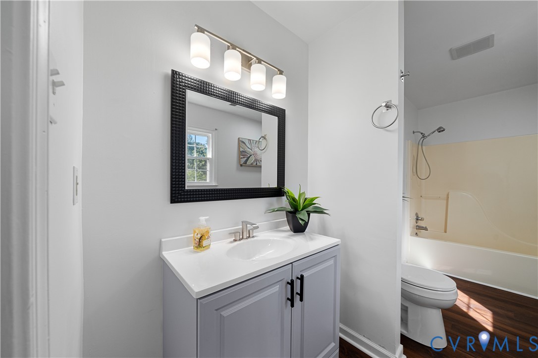 Bathroom vanity with gray cabinets and black-framed mirror, beside a toilet and cream-colored tub-shower.