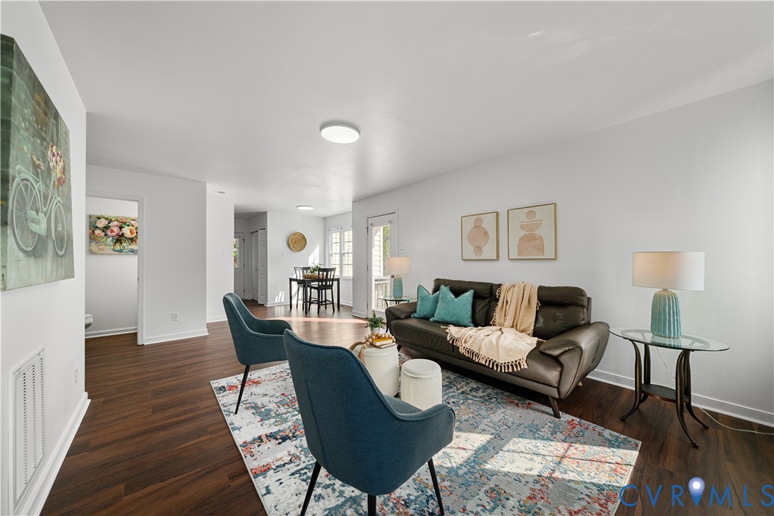 Staged living room with a brown leather sofa, teal chairs, and dark wood floors.