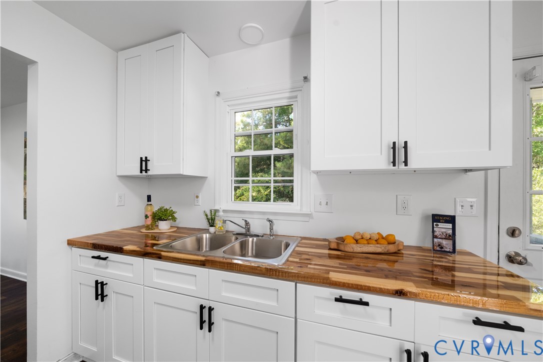 Bright kitchen with white cabinets, butcher-block counters, and a double-basin sink beneath a window.