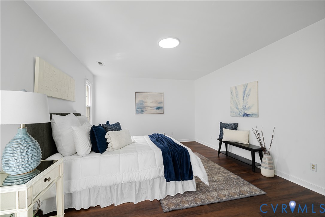 Staged bedroom with a white bed, navy accents, patterned rug, and dark wood floors.