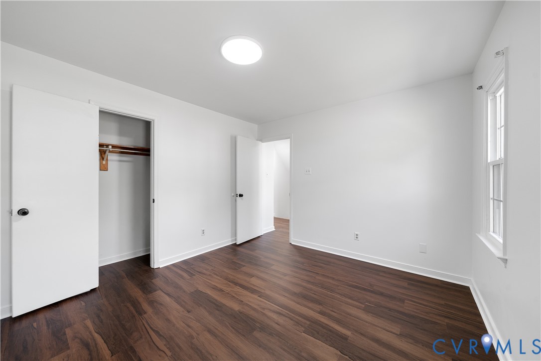 Empty bedroom with dark wood-look floors, an open closet, and a tall window.