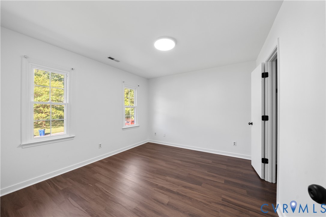 Vacant bedroom with dark wood floors and two windows.