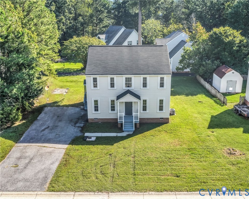 Aerial view of a white two-story house with a driveway, broad lawn, and detached shed.