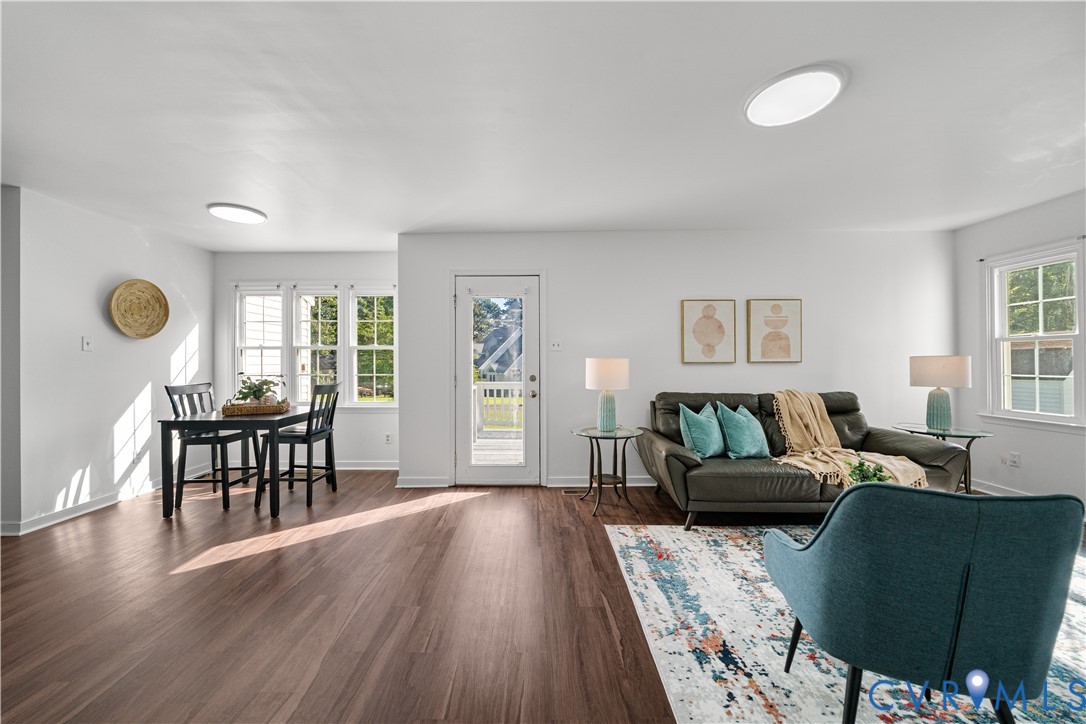 Open-plan living and dining room with dark wood floors, a leather sofa, and turquoise accent chairs.