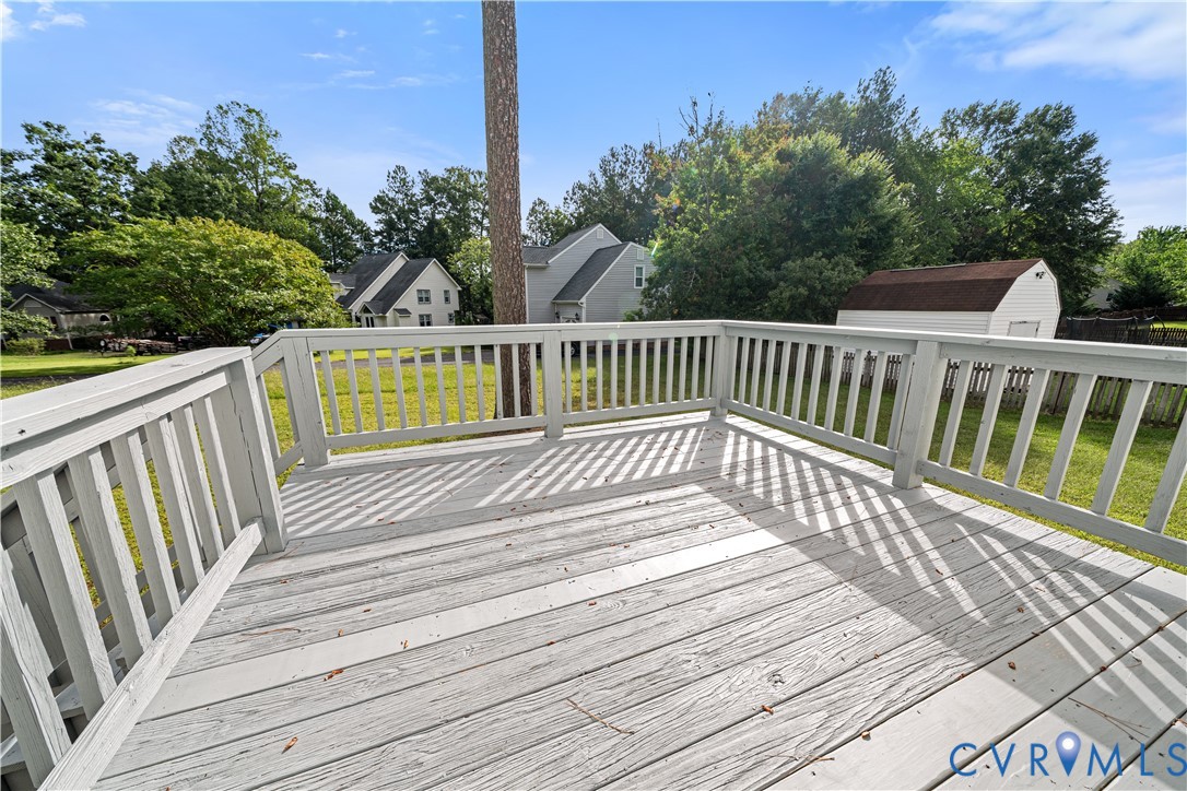 White wooden deck overlooking a green backyard, with trees and neighboring houses beyond.