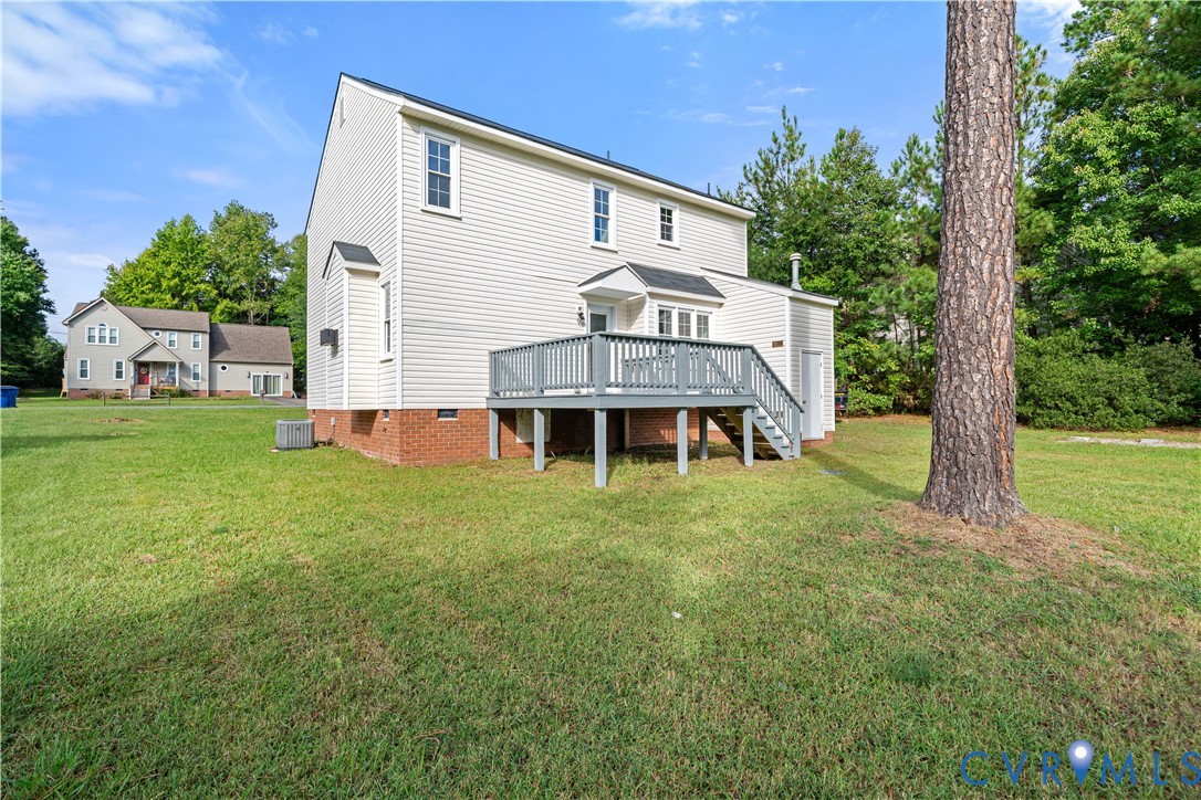 Two-story white house with a raised gray deck, brick foundation, and spacious lawn.