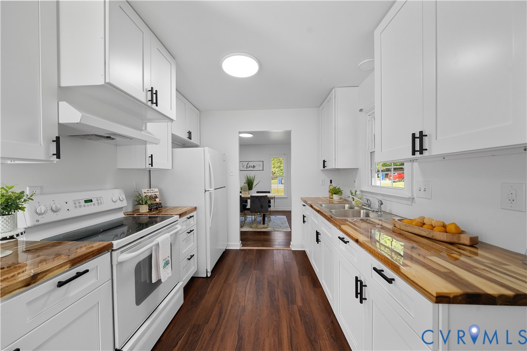 Bright white kitchen with butcher-block counters, dark wood floors, and a view into the dining area.