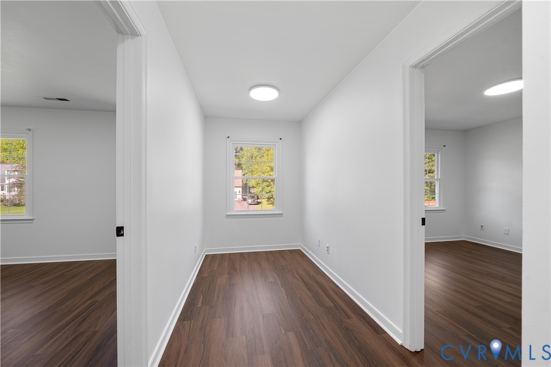 Empty room with dark wood-look flooring, a window, and open doorways to adjoining rooms.