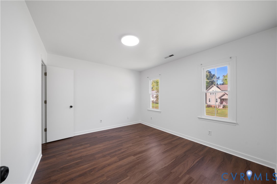 Vacant bedroom with dark wood-look floors, white walls, and two windows.