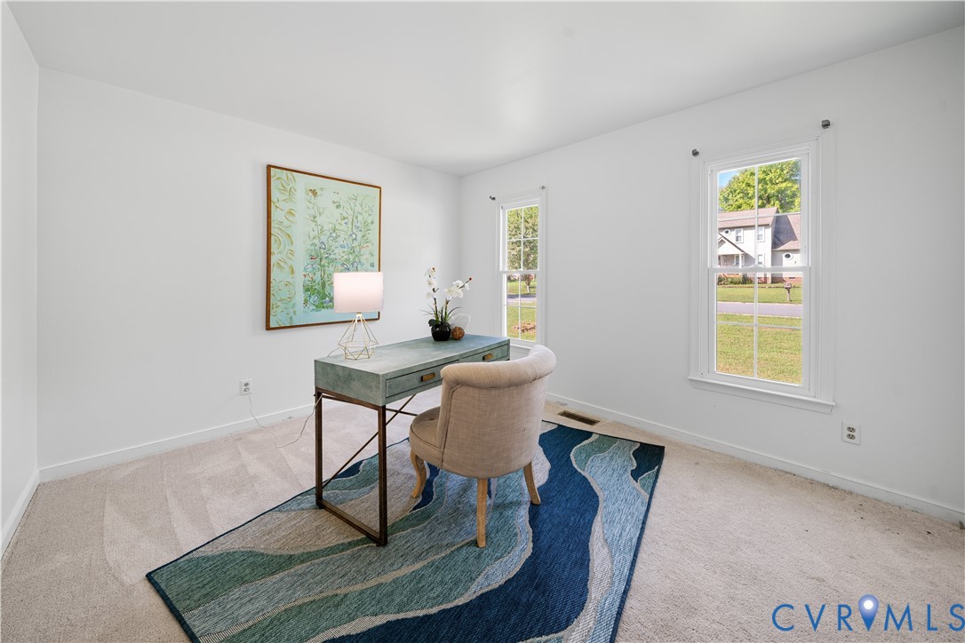Home office with a green desk, upholstered chair, blue patterned rug, and two bright windows.