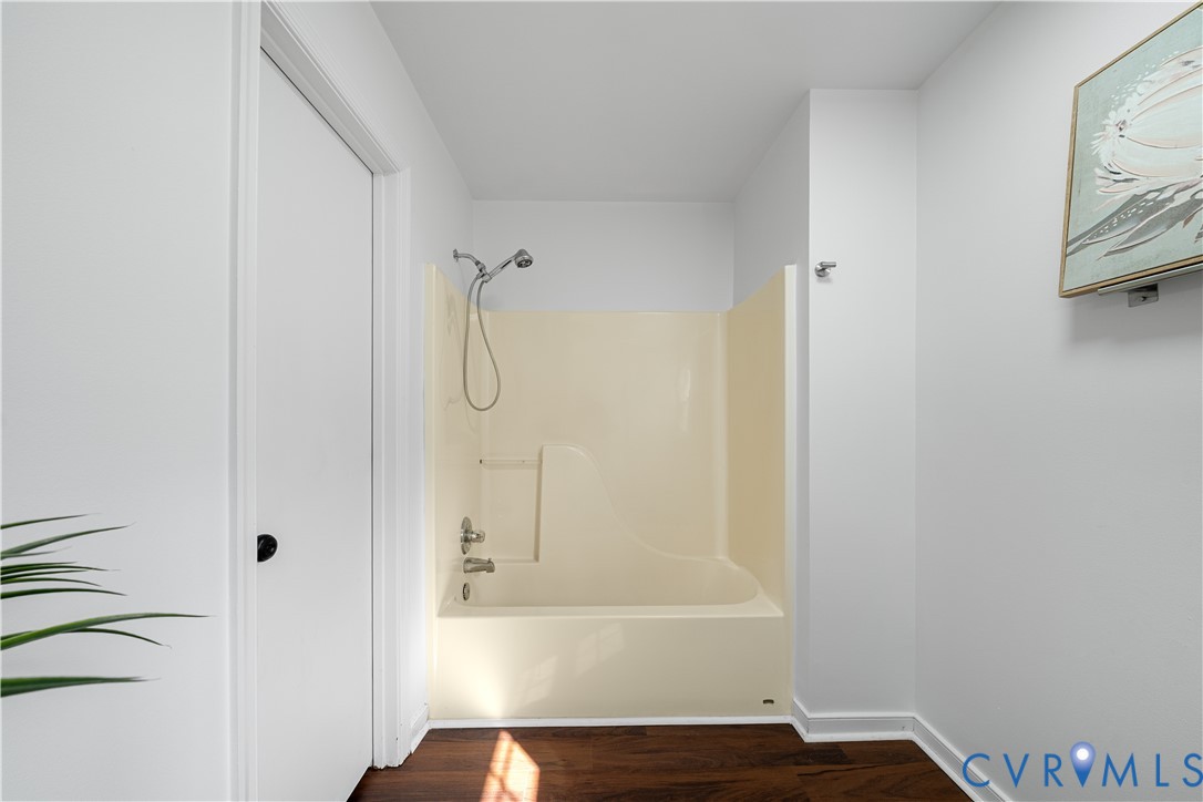Bathroom with a cream tub and shower surround, handheld showerhead, and dark wood flooring.
