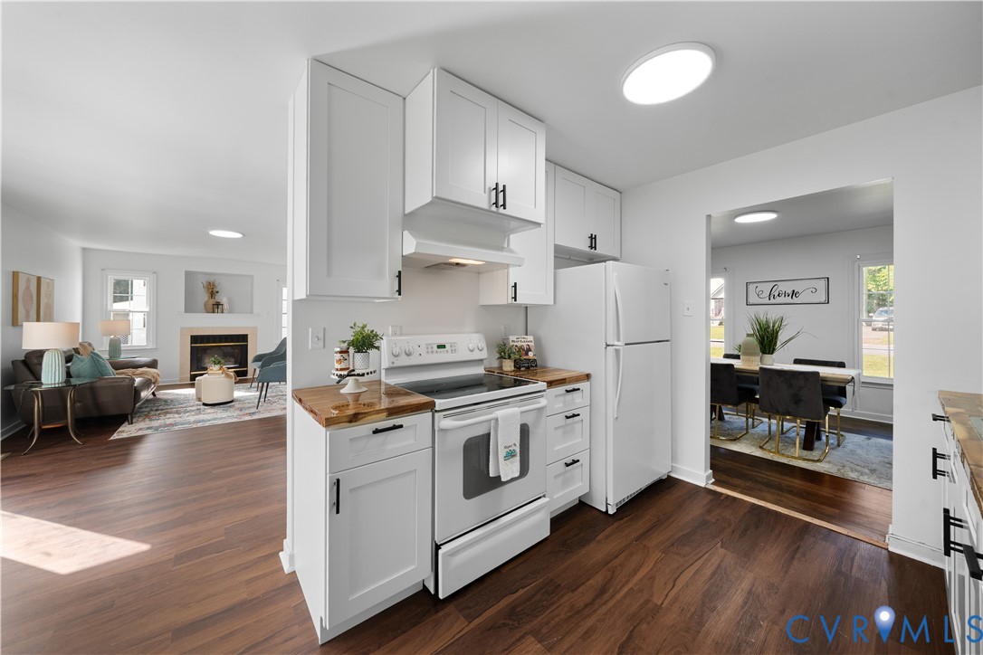 Open-plan kitchen with white cabinetry, stainless steel appliances, and butcher-block countertops beside living and dining areas.
