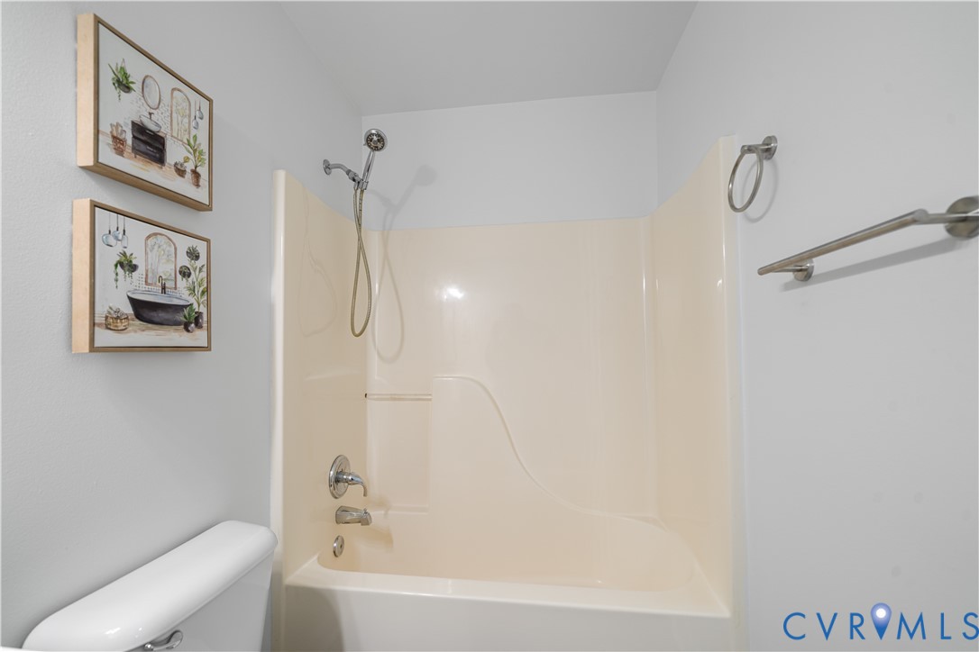 Bathroom tub and shower with chrome fixtures and framed artwork.