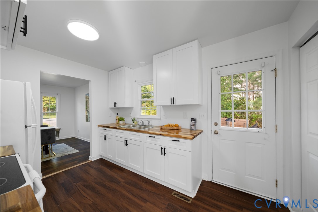 Bright white kitchen with butcher-block counters, dark wood floors, and a windowed exterior door.