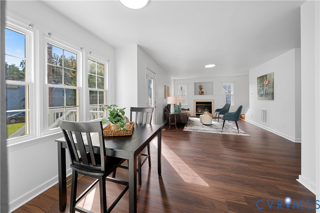 Open-plan living and dining room with tall windows, dark hardwood floors, and a fireplace.
