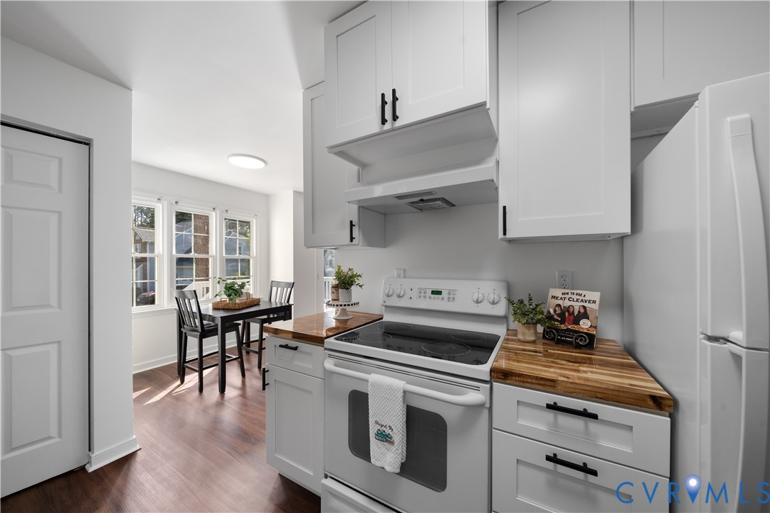 Kitchen with white cabinets, butcher-block counters, and a dining nook by three windows.