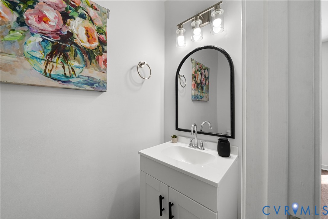 Bathroom vanity with a white sink, arched black-framed mirror, and colorful floral artwork.