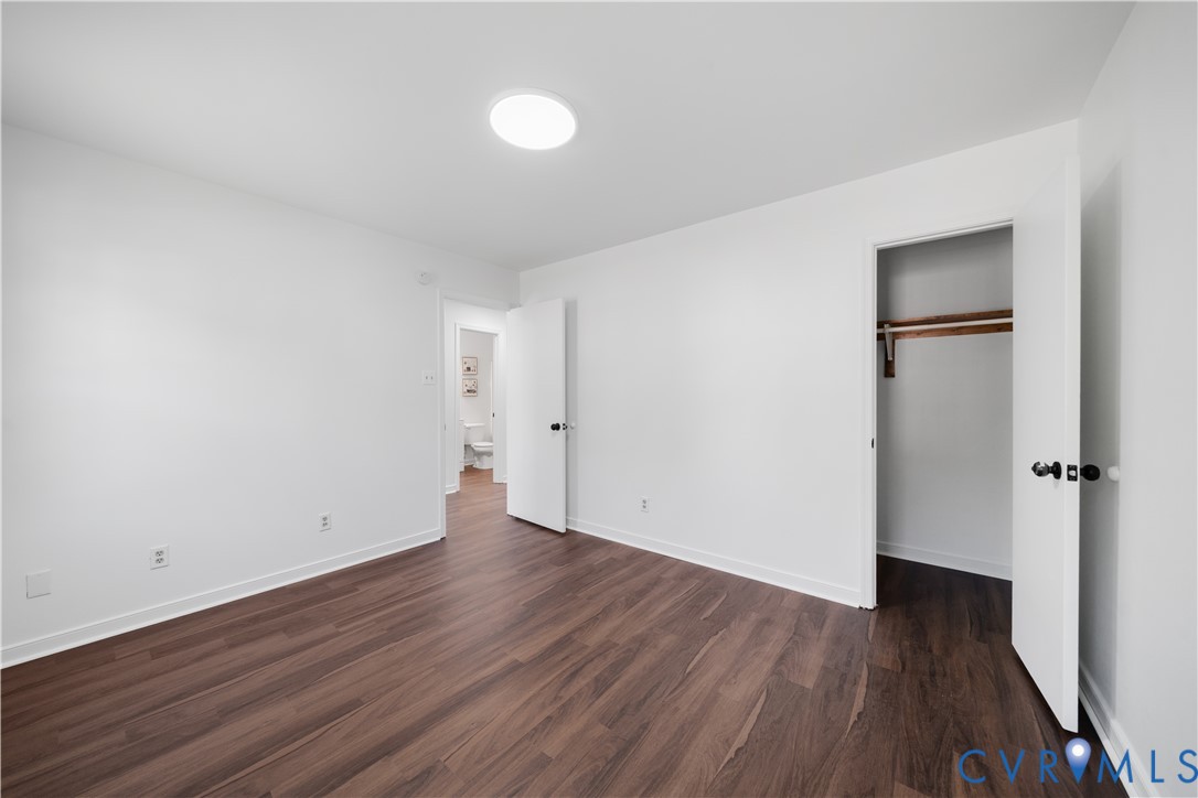 Empty bedroom with dark wood-look flooring, an open closet, and a doorway to the bathroom.