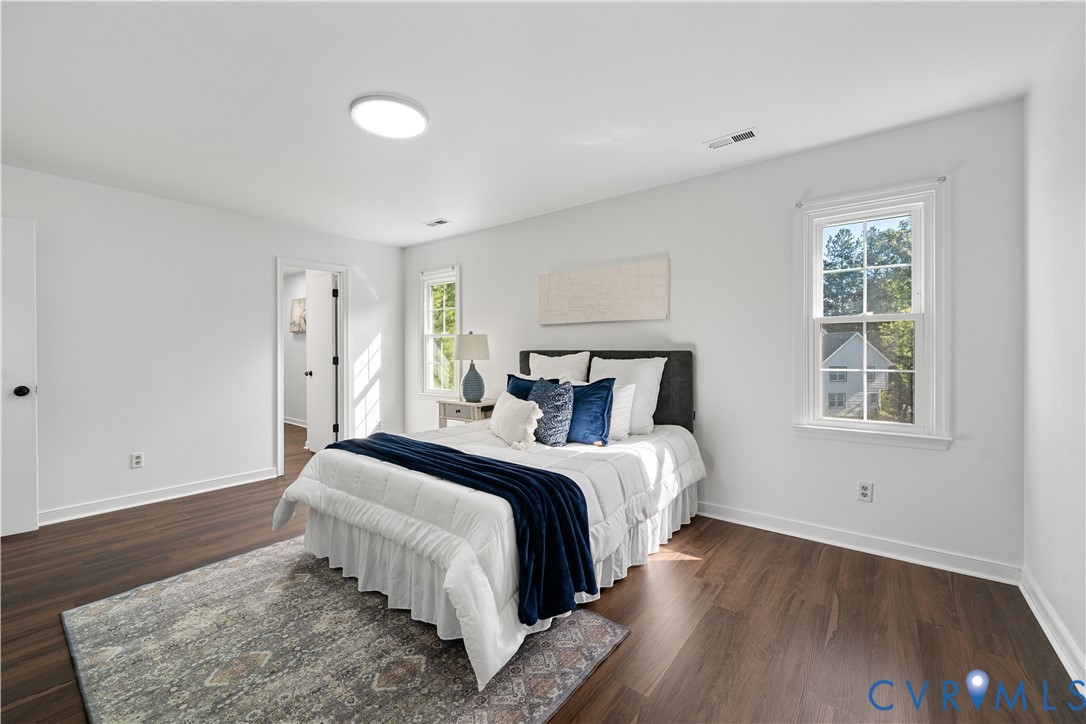 Staged bedroom with a white bed, navy blue bedding, hardwood floors, and two windows.