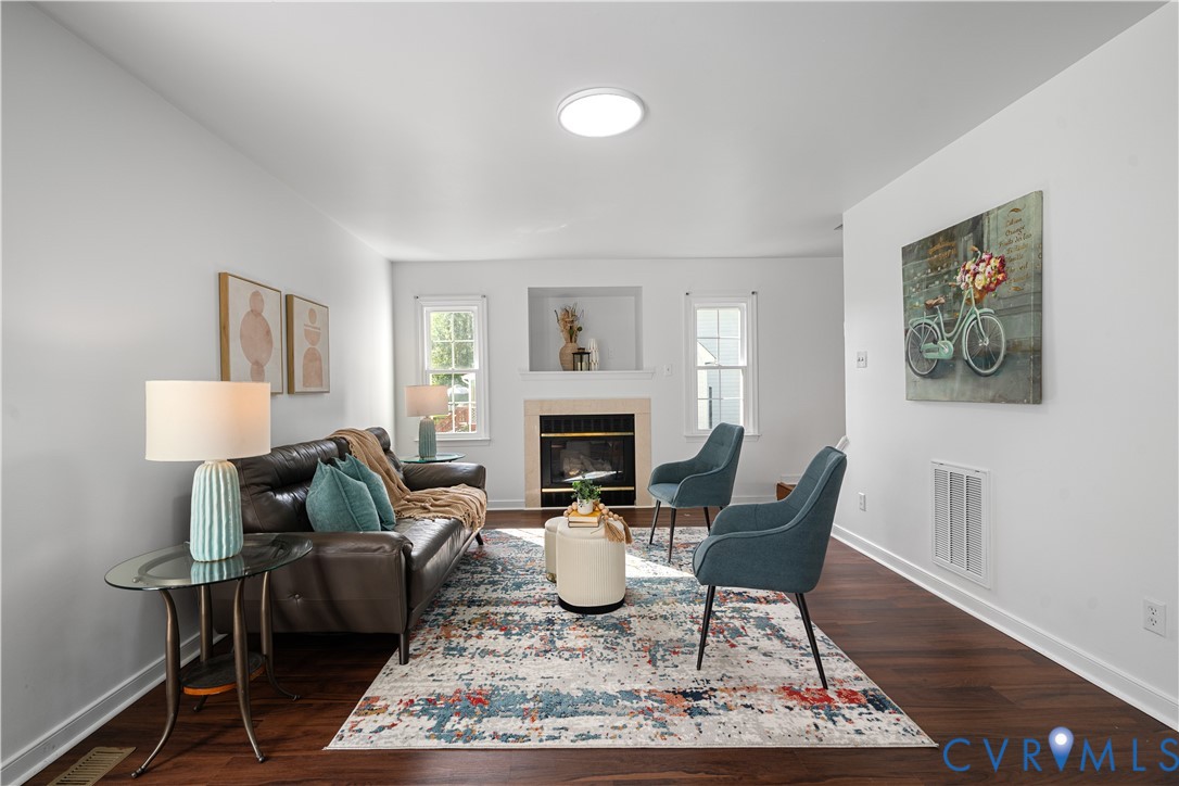 Staged living room with a fireplace, leather sofa, teal chairs, and patterned rug.