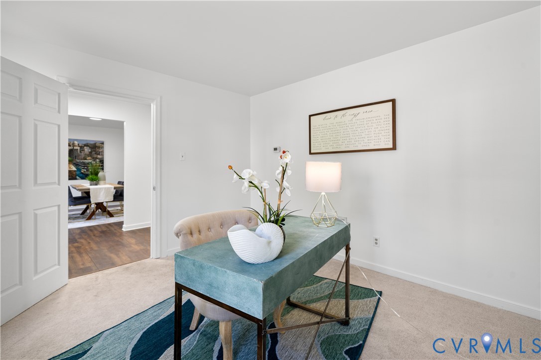 Staged home office with a teal desk, orchid, and upholstered chair beside an open doorway.