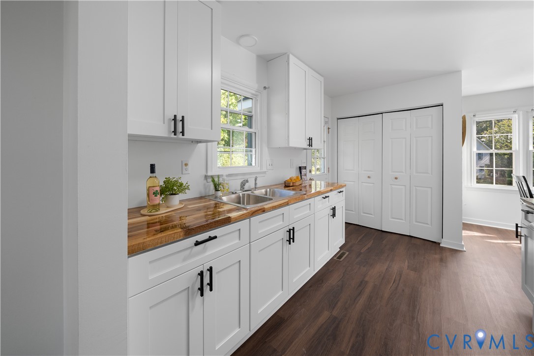 Kitchen with white cabinetry, butcher-block counters, a double-basin sink, and dark wood flooring.