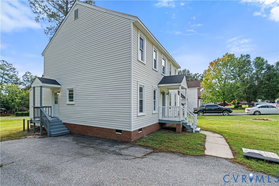 Two-story light-sided house with brick foundation, gray entry steps, and a curved walkway.