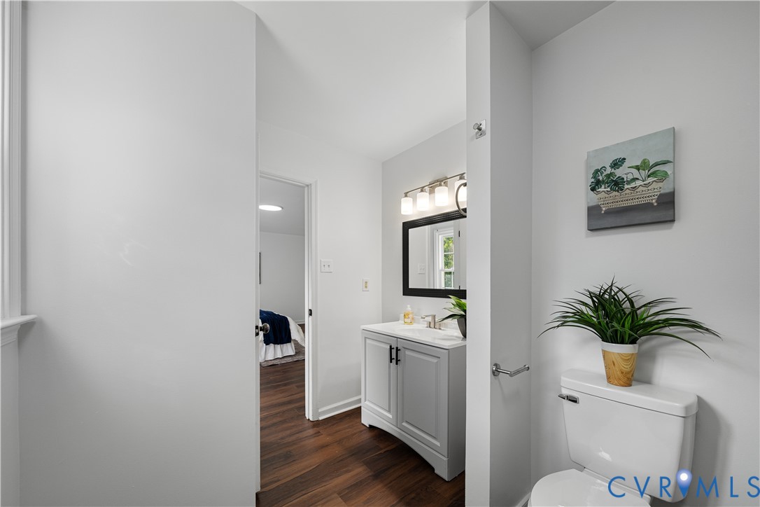 Bathroom with a gray vanity and black-framed mirror, viewed past a toilet toward a bedroom.