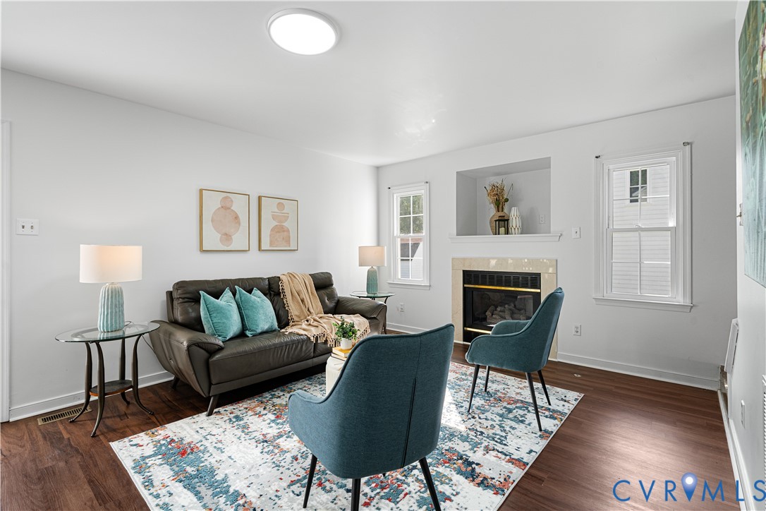 Staged living room with teal chairs, a leather sofa, a fireplace, and a colorful patterned rug.