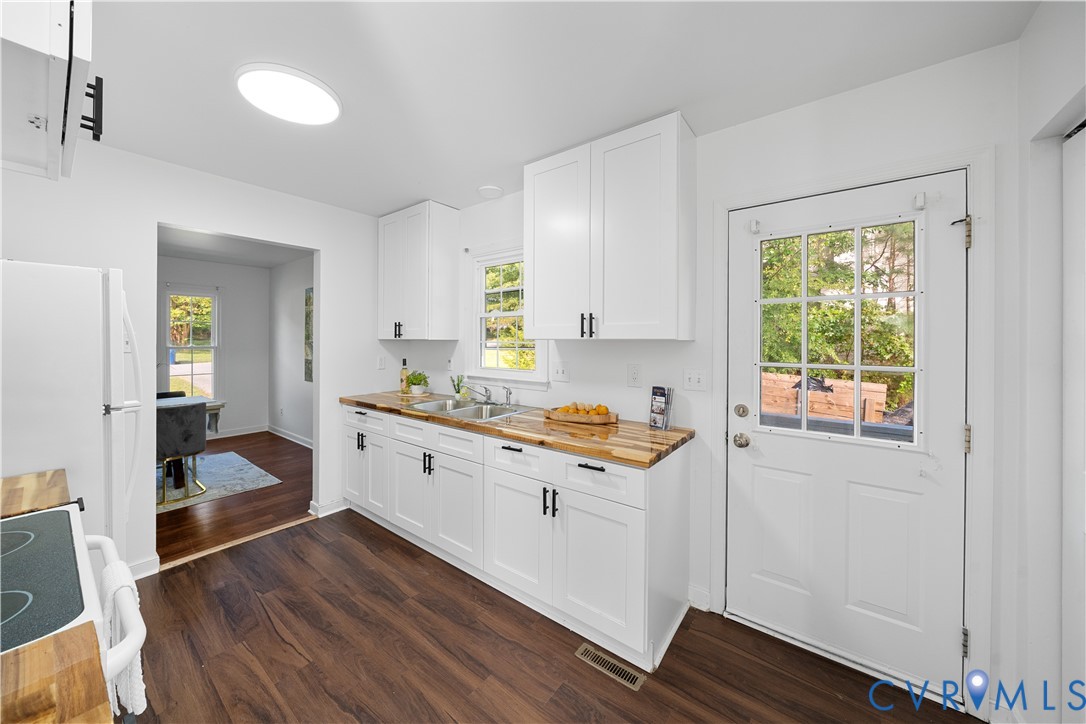 Bright kitchen with white cabinets, butcher-block counters, and dark wood floors.
