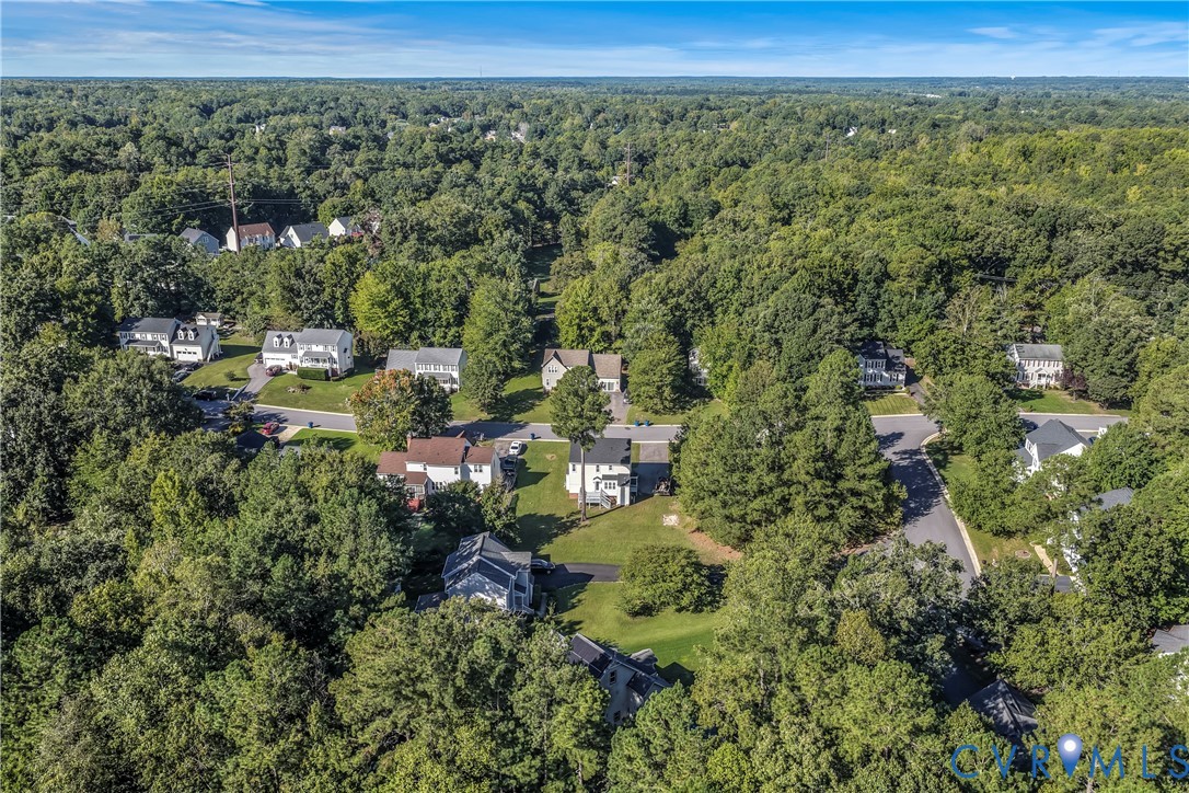 Aerial view of a wooded neighborhood with detached homes and winding residential streets.