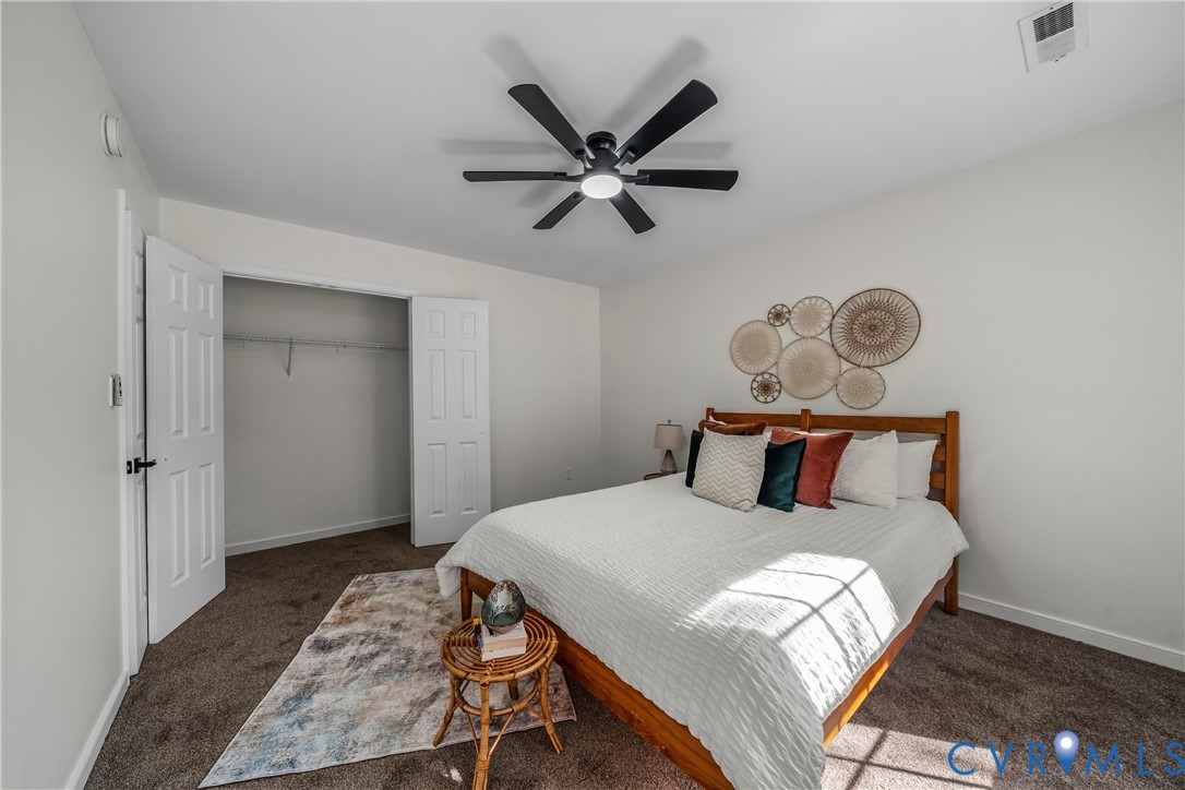 Staged bedroom with a wooden bed, white bedding, ceiling fan, and open closet.