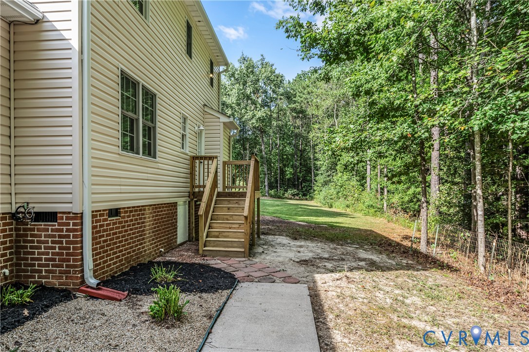 House side with wooden steps and a concrete walkway leading toward a wooded yard.
