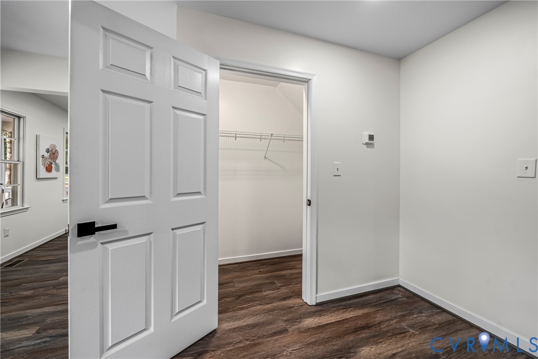 Vacant room with dark wood flooring and an open closet with a wire shelf and hanging rod.