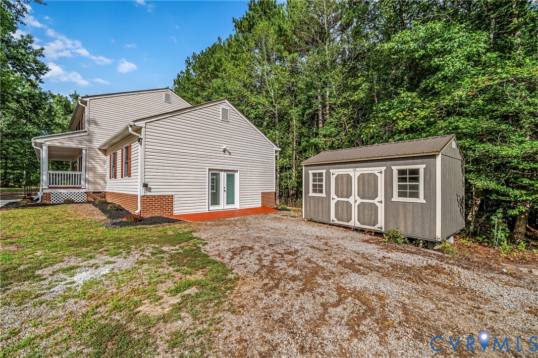 House with covered porch and detached gray storage shed beside a gravel drive.