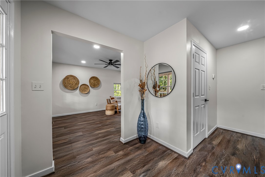 Entry foyer with dark wood-look floors, a white front door, and a tall blue vase beneath a round mirror.