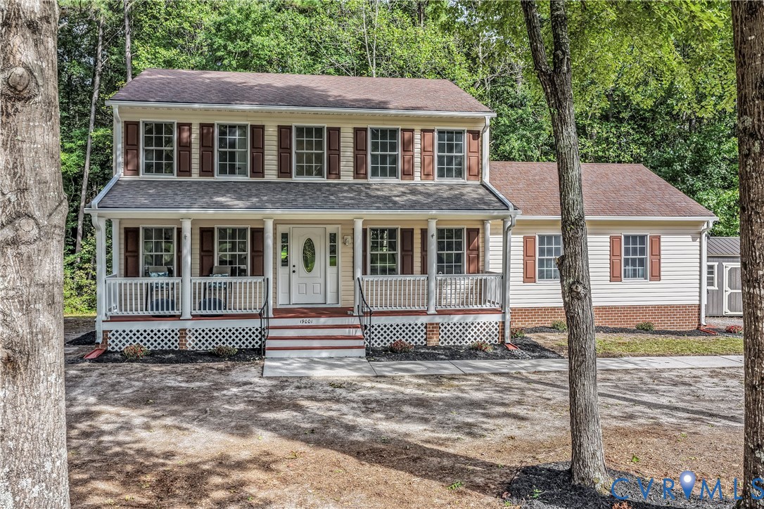 Two-story house with a covered porch, dark shutters, and mature trees framing the front.