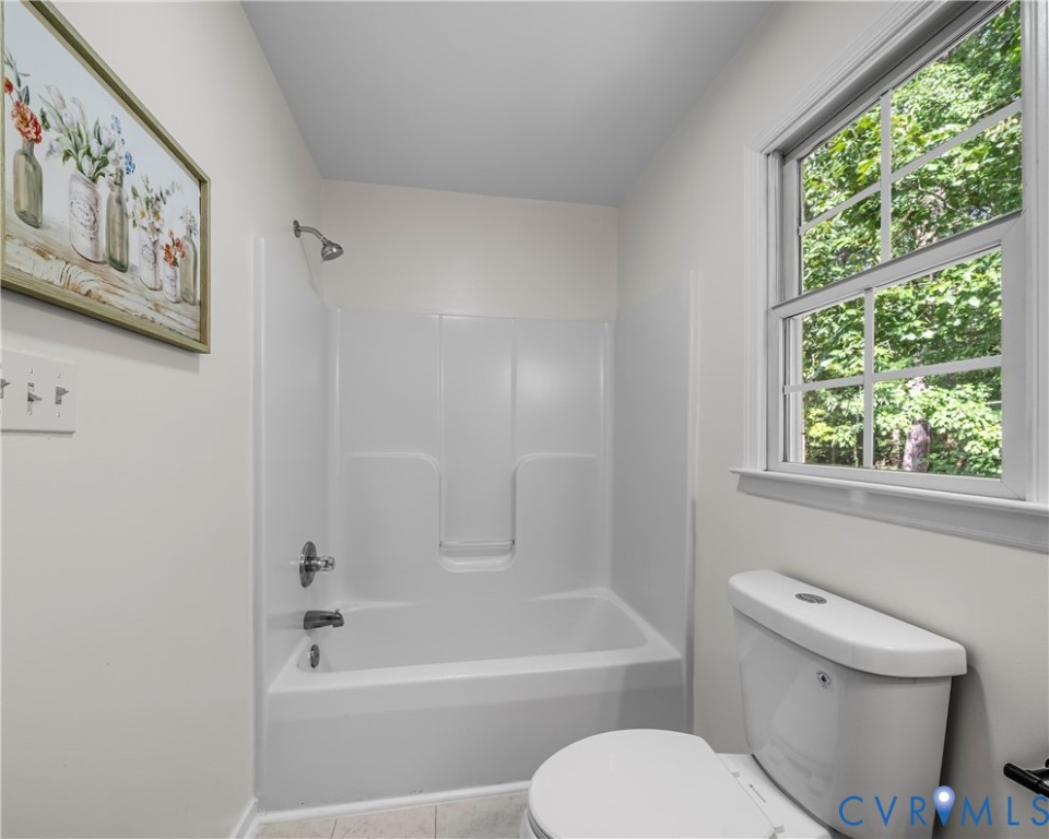 Bathroom with a white tub-shower, toilet, and large window overlooking green foliage.