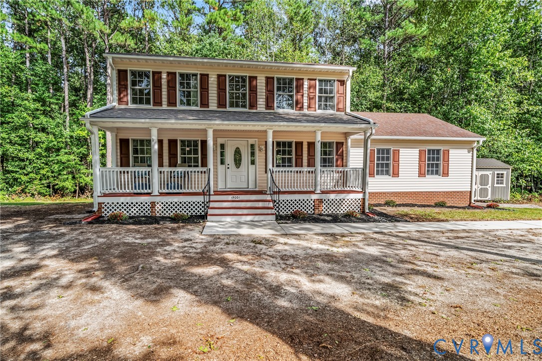 Two-story house with a columned front porch, red-brown shutters, and trees behind it.