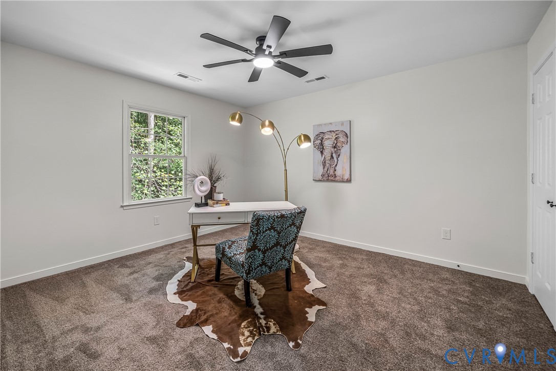 Furnished home office with a white desk, patterned chair, cowhide rug, and window overlooking greenery.