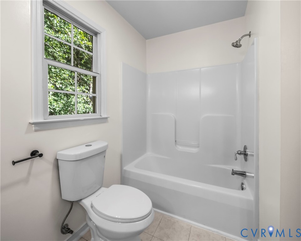 Bathroom with a white tub and shower, toilet, and window overlooking greenery.