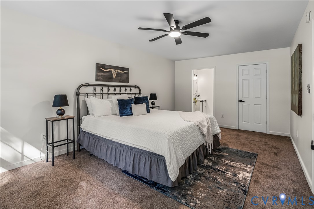 Staged bedroom with a large white bed, black metal headboard, blue pillows, and ceiling fan.