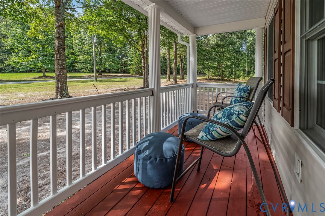 Covered porch with red wood flooring, white railings, and blue-cushioned chairs overlooking a tree-lined yard.