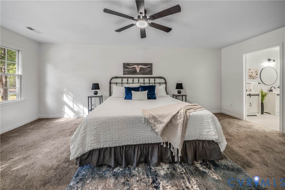 Staged primary bedroom with a king-size bed, ceiling fan, and adjoining bathroom doorway.
