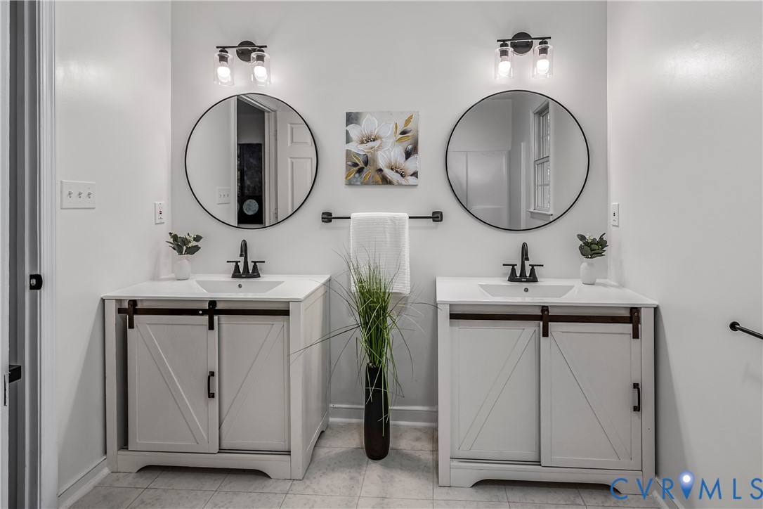 Bathroom with two white vanities, round mirrors, black faucets, and a tall plant between the sinks.