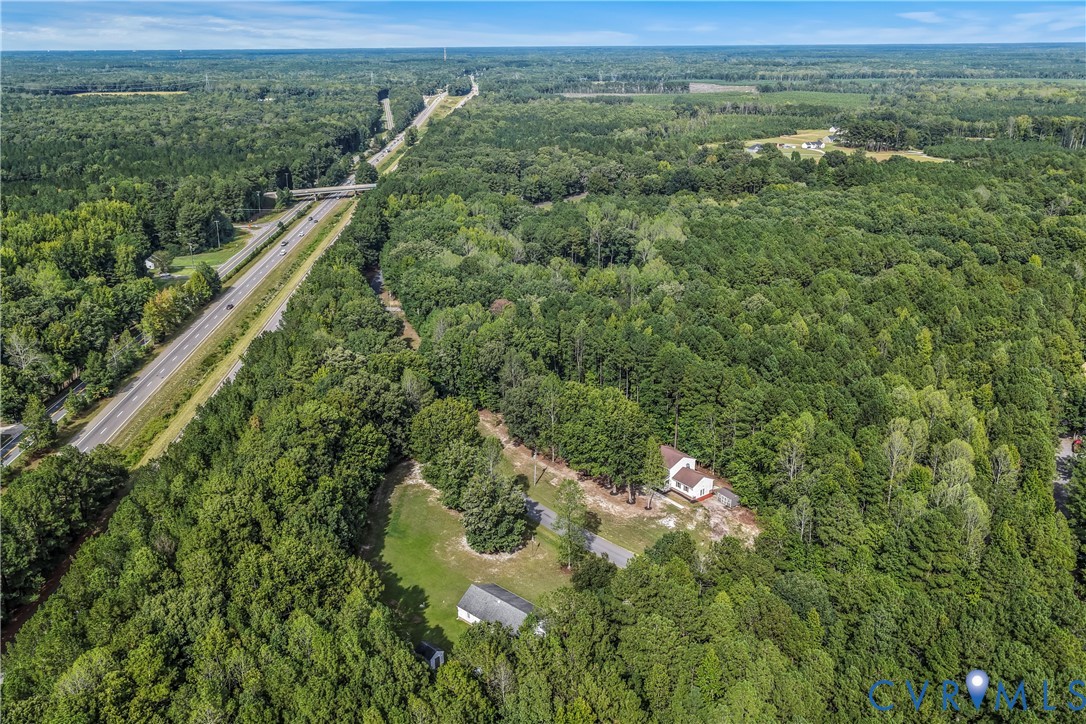 Aerial view of a house and outbuildings surrounded by woodland, with a divided highway nearby.