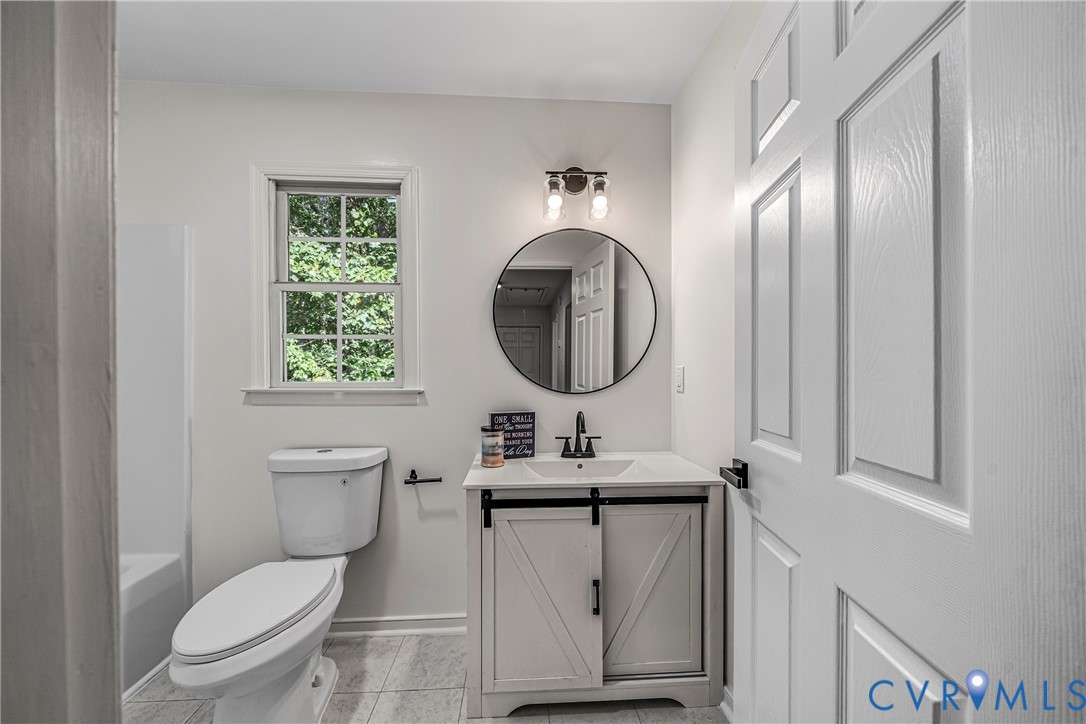 Bathroom with a gray barn-door vanity, round mirror, and window overlooking green foliage.