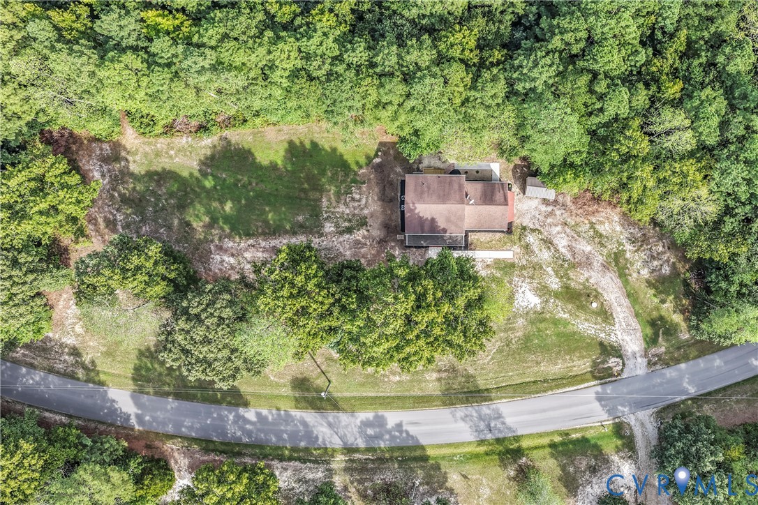 Aerial view of a house surrounded by trees, with a long driveway and road frontage.