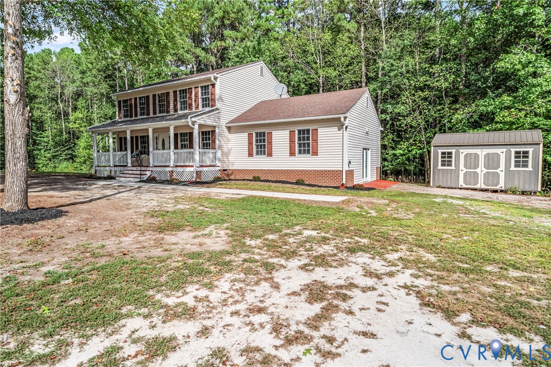 Two-story home with a covered porch and detached shed amid surrounding trees.