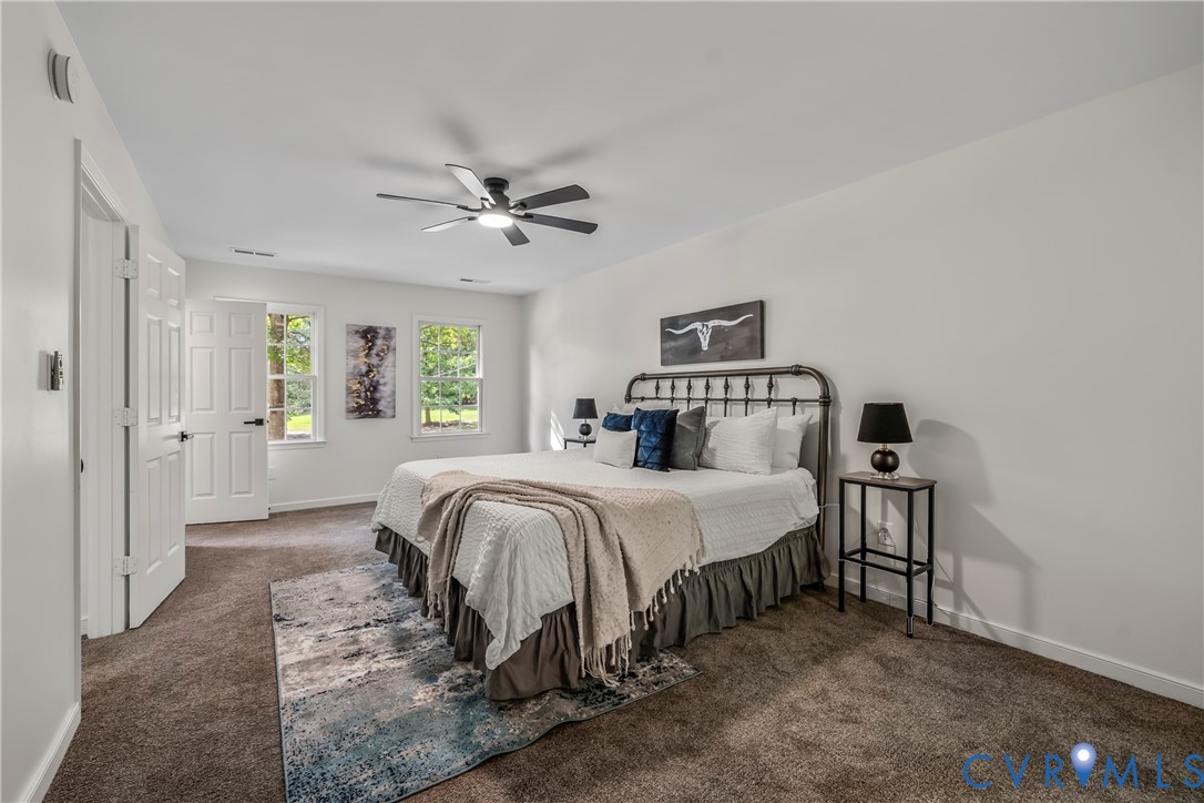 Bedroom with a metal-frame bed, blue accent pillows, patterned rug, and two windows overlooking greenery.